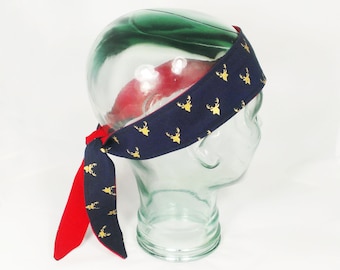 May include: A navy blue headband with a red trim and a gold deer print. The headband is tied in a knot at the back.