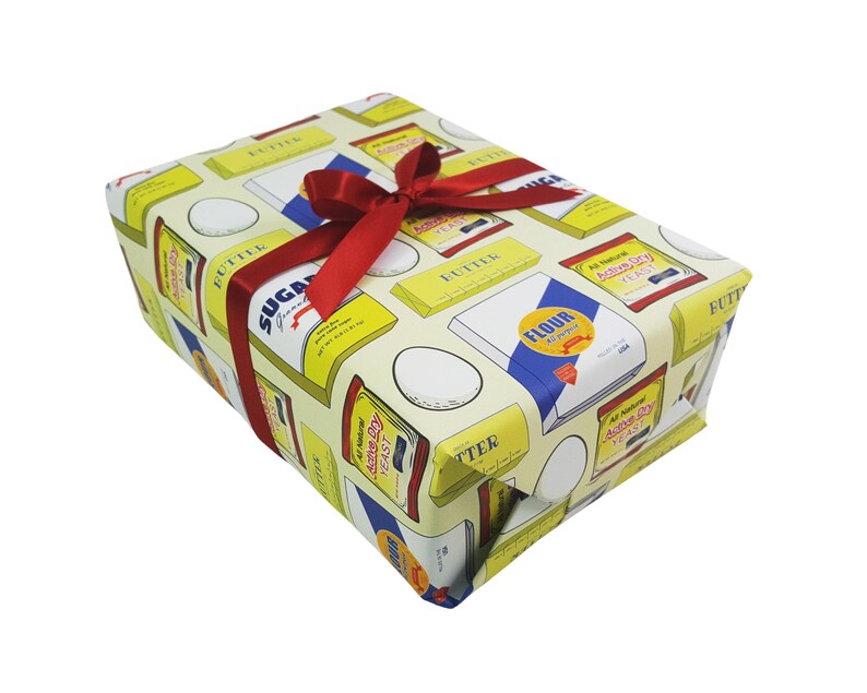 Puede incluir: Papel de regalo amarillo con una cinta roja y un patr&oacute;n de varios ingredientes para hornear, incluyendo huevos, harina, az&uacute;car y mantequilla. El texto en el papel de regalo incluye "All Natural Active Dry Yeast" y "Flour All Purpose".