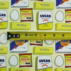 Puede incluir: Una tela de patr&oacute;n amarillo y blanco con varios ingredientes para hornear, que incluyen mantequilla, az&uacute;car, harina y levadura. La tela presenta un patr&oacute;n repetitivo de cajas con ilustraciones de los ingredientes y sus nombres. Una cinta m&eacute;trica amarilla se coloca sobre la tela.