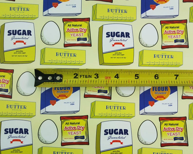 Puede incluir: Una tela de patr&oacute;n amarillo y blanco con varios ingredientes para hornear, que incluyen mantequilla, az&uacute;car, harina y levadura. La tela presenta un patr&oacute;n repetitivo de cajas con ilustraciones de los ingredientes y sus nombres. Una cinta m&eacute;trica amarilla se coloca sobre la tela.