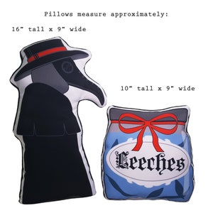 May include: Two decorative cushions, one shaped like a plague doctor wearing a black robe and a black hat with a red band, and the other shaped like a blue jar with a red bow and the word "Leeches" in white lettering. The plague doctor cushion is 16 inches tall and 9 inches wide. The jar cushion is 10 inches tall and 9 inches wide.