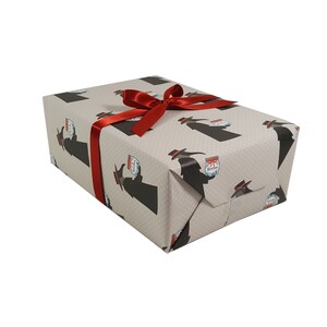 May include: A gift box wrapped in gray wrapping paper with a black and white pattern of a person holding a jar. The box is tied with a red ribbon.