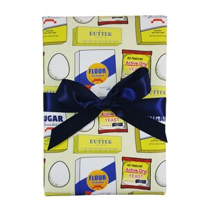 Puede incluir: Papel de regalo amarillo y azul con un patr&oacute;n de mantequilla, harina, az&uacute;car, huevos y levadura. El papel est&aacute; atado con una cinta azul.