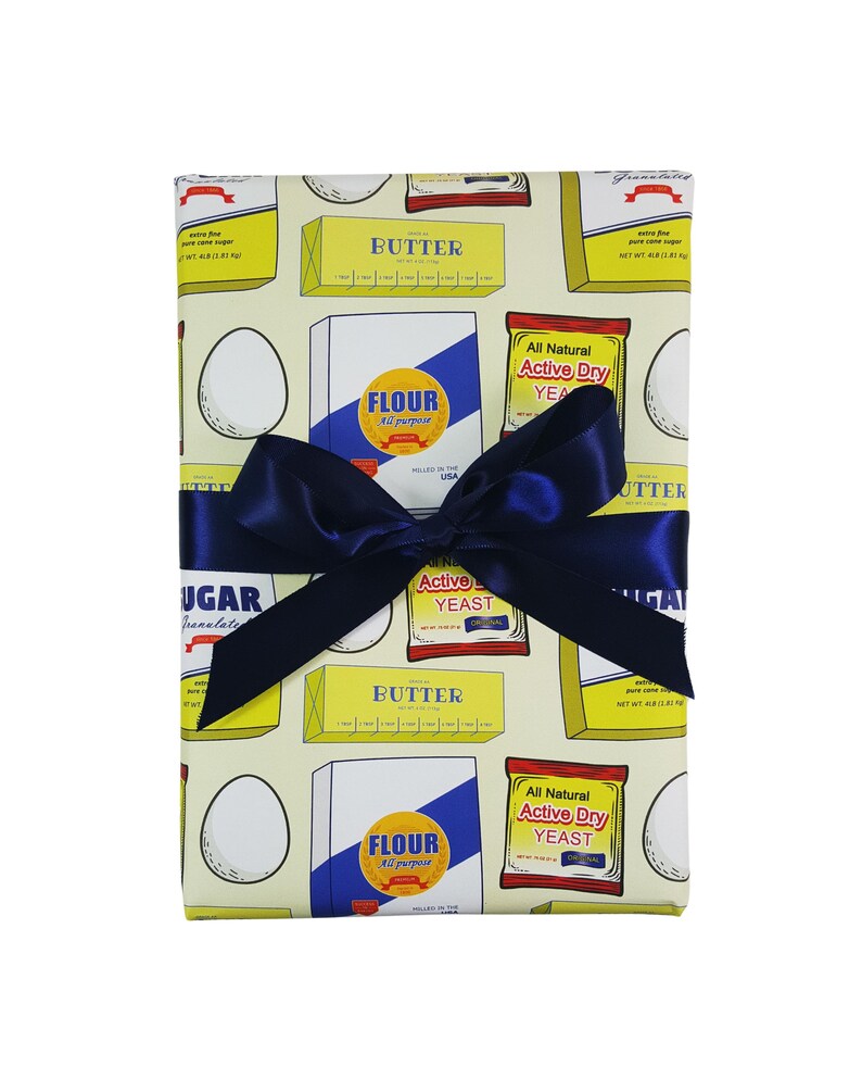 Puede incluir: Papel de regalo amarillo y azul con un patr&oacute;n de mantequilla, harina, az&uacute;car, huevos y levadura. El papel est&aacute; atado con una cinta azul.