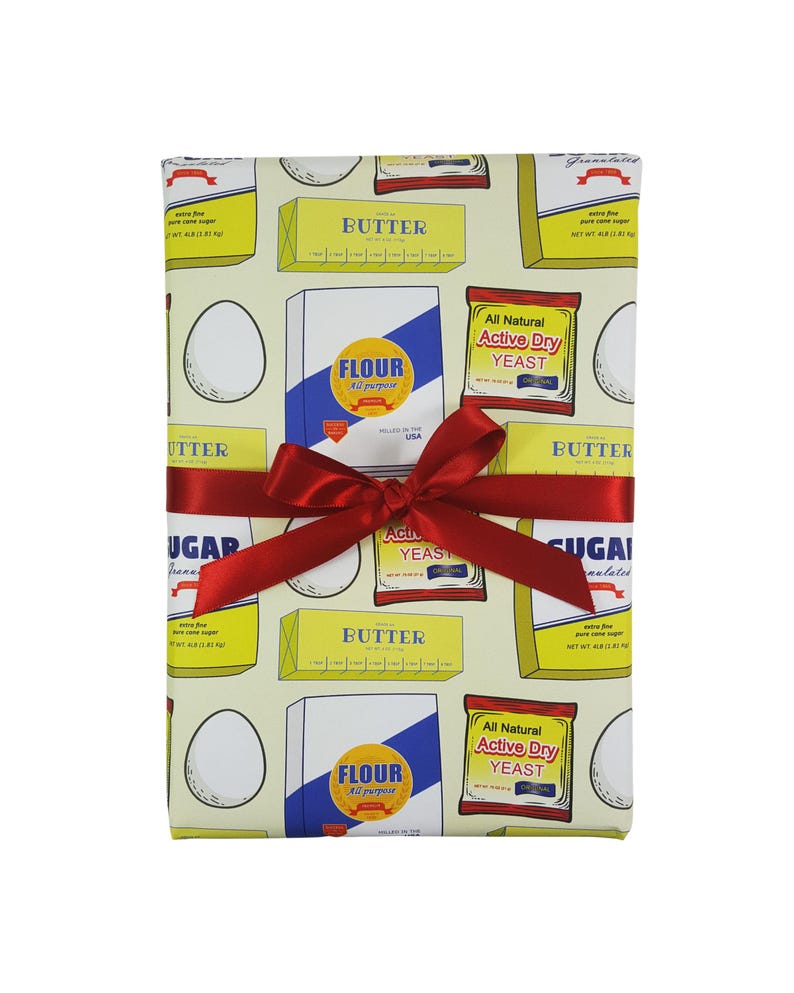 Puede incluir: Papel de regalo amarillo y blanco con un patr&oacute;n repetido de alimentos b&aacute;sicos de cocina, que incluyen mantequilla, harina, az&uacute;car y levadura. El papel est&aacute; atado con una cinta roja.