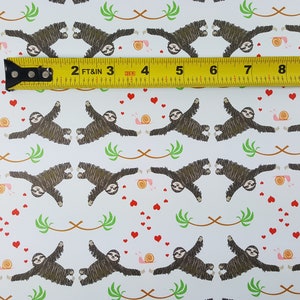 May include: A white background with a repeating pattern of brown sloths hanging upside down with their arms outstretched. The sloths are surrounded by small red hearts, pink snails, and green palm leaves. A yellow measuring tape is placed across the top of the image with the numbers 2, 3, 4, 5, 6, 7, 8, and 9 visible.
