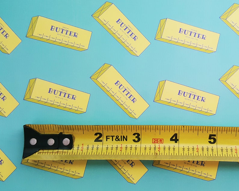 May include: A repeating pattern of yellow butter boxes with the word "BUTTER" in purple on a light blue background. A yellow tape measure is in the foreground, showing measurements in feet and inches.