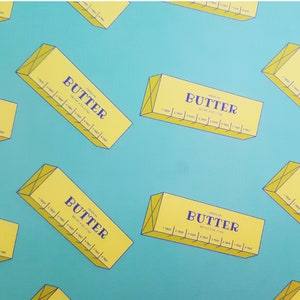 May include: A pattern of yellow butter boxes with the word "BUTTER" in navy blue, set against a teal background. Each box has measurement markings. The boxes are oriented at various angles.
