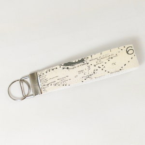 May include: A white fabric keychain with a black and white map print. The map shows the Hawaiian Islands and the text "Tropic of Cancer". The keychain has a silver key ring.