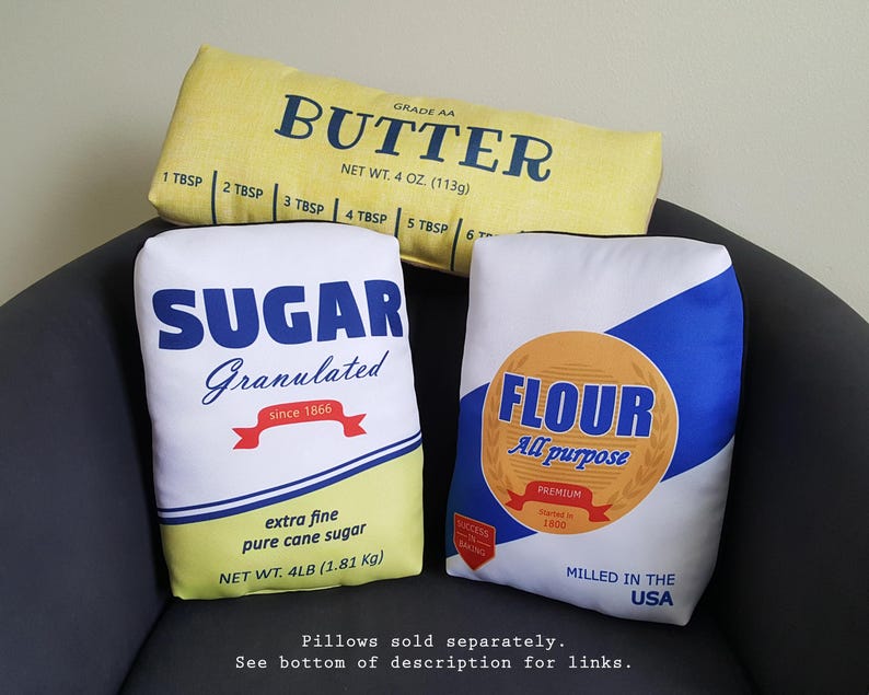 Puede incluir: Tres almohadas decorativas con un dise&ntilde;o vintage de empaque de alimentos. Las almohadas son amarillas, blancas y azules. La almohada amarilla dice "Grade AA Butter" con medidas en onzas. La almohada blanca dice "Sugar Granulated" con medidas en libras. La almohada azul dice "Flour All Purpose" con medidas en libras.