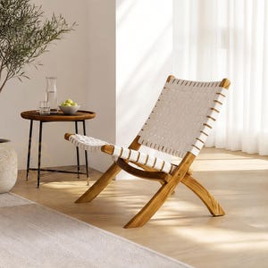 May include: A lounge chair featuring a natural wood frame with a crisscross base and a seat and backrest constructed from woven white straps. The chair is positioned at an angle, showcasing its low-profile design and the contrast between the wood and white.