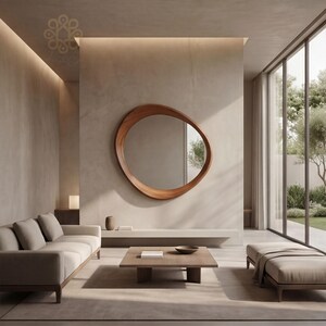 May include: An asymmetrical, organic-shaped wall mirror with a smooth, polished wooden frame. The mirror is mounted on a plain, light-coloured wall above a low, horizontal shelf in a room with a sofa, a square wooden coffee table, and a bench.