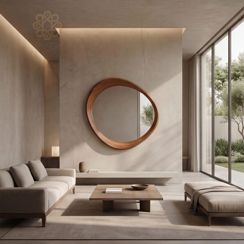 May include: An asymmetrical, organic-shaped wall mirror with a smooth, polished wooden frame. The mirror is mounted on a plain, light-coloured wall above a low, horizontal shelf in a room with a sofa, a square wooden coffee table, and a bench.