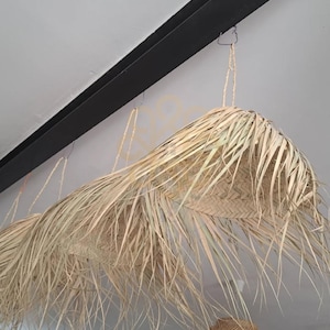 May include: Natural woven pendant lamps hanging from a black beam. The lampshades are made of woven palm leaves, creating a warm glow. The design is perfect for adding a touch of bohemian style to any room. The lamps are suspended from the ceiling.