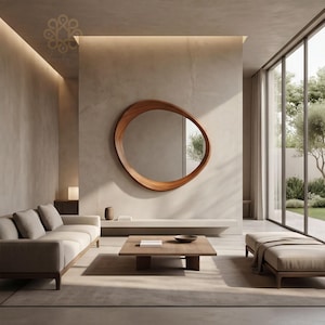 May include: An irregular, organic-shaped wooden wall mirror with a warm brown finish mounted on a smooth beige wall. The mirror reflects a bright outdoor scene with trees, positioned above a low, horizontal shelf and a square wooden coffee table.