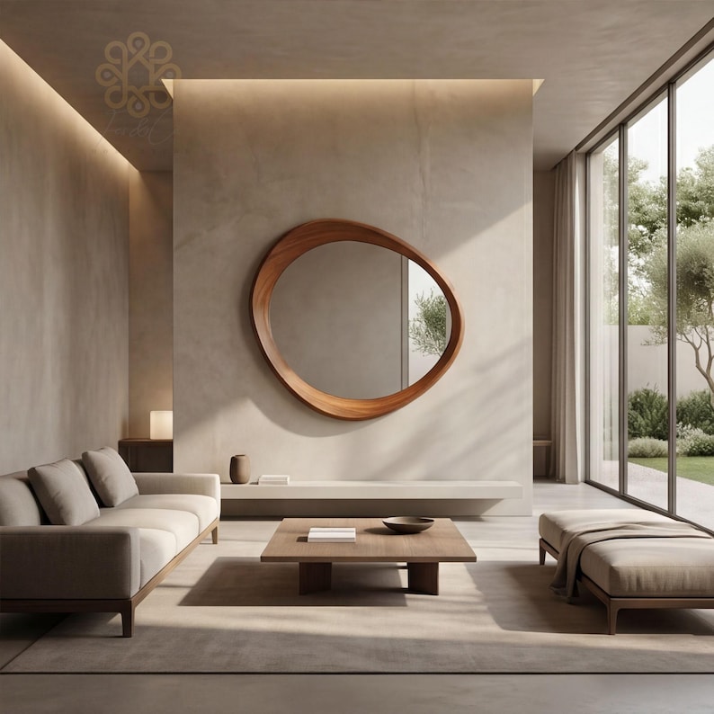 May include: An irregular, organic-shaped wooden wall mirror with a warm brown finish mounted on a smooth beige wall. The mirror reflects a bright outdoor scene with trees, positioned above a low, horizontal shelf and a square wooden coffee table.
