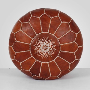 May include: A brown leather pouf with white stitching and a white embroidered star design.