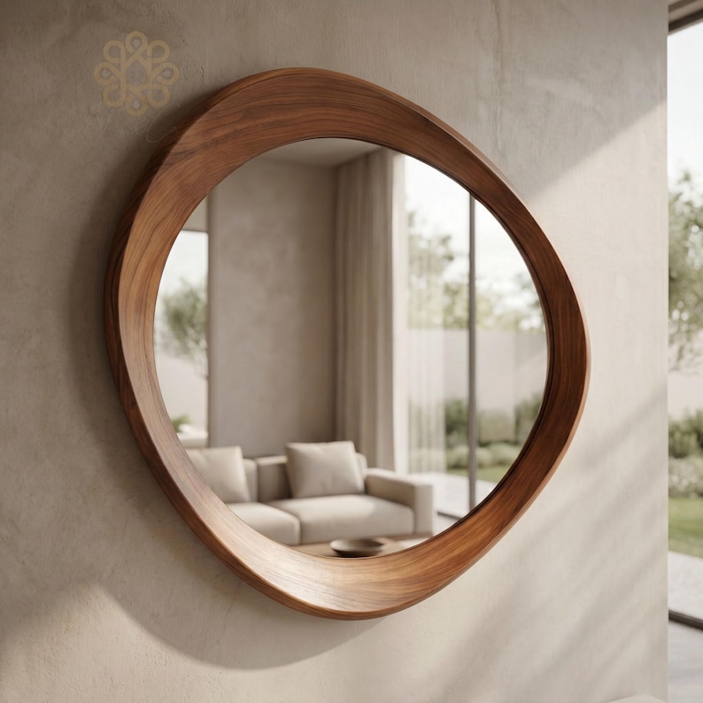 May include: A wall-mounted mirror featuring an organic, asymmetrical, rounded wooden frame with a smooth, polished brown grain finish. The reflective glass surface captures a view of a living room interior with a sofa and window light.