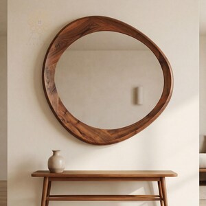 May include: A large, organic-shaped wall mirror with a thick, polished dark brown wooden frame featuring a visible natural wood grain pattern. The mirror has an asymmetrical, rounded silhouette and is mounted on a plain, light-coloured wall.
