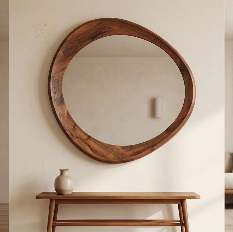 May include: A large, organic-shaped wall mirror with a thick, polished dark brown wooden frame featuring a visible natural wood grain pattern. The mirror has an asymmetrical, rounded silhouette and is mounted on a plain, light-coloured wall.