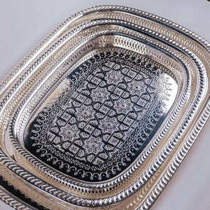 May include: A set of three silver oval serving trays with intricate embossed designs. The trays are nested together, with the largest tray on the bottom and the smallest tray on top.