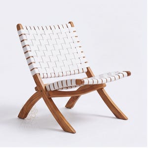 May include: A folding chair featuring a natural light brown wooden frame and a seat and backrest constructed from white woven straps. The chair has a low-profile design with crossed legs and a slanted back, showcasing a clear wood grain finish.