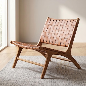 May include: A low-profile lounge chair featuring a light brown wooden frame and a seat and backrest constructed from woven tan leather straps. The chair has a slanted back and four angled legs connected by horizontal support bars.