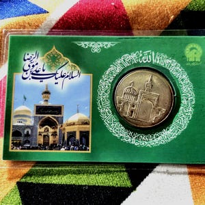 May include: A gold coin depicting a domed building and minarets, presented in a green card with Arabic calligraphy and a mosque image. The card is encased in a clear plastic sleeve.