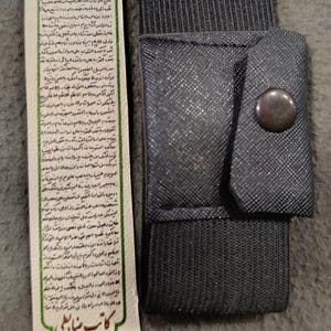 May include: A dark gray fabric pouch with a snap closure and an elastic band, next to a decorative bookmark. The bookmark has text in a foreign language, with floral and geometric designs in pink, green, and gold.