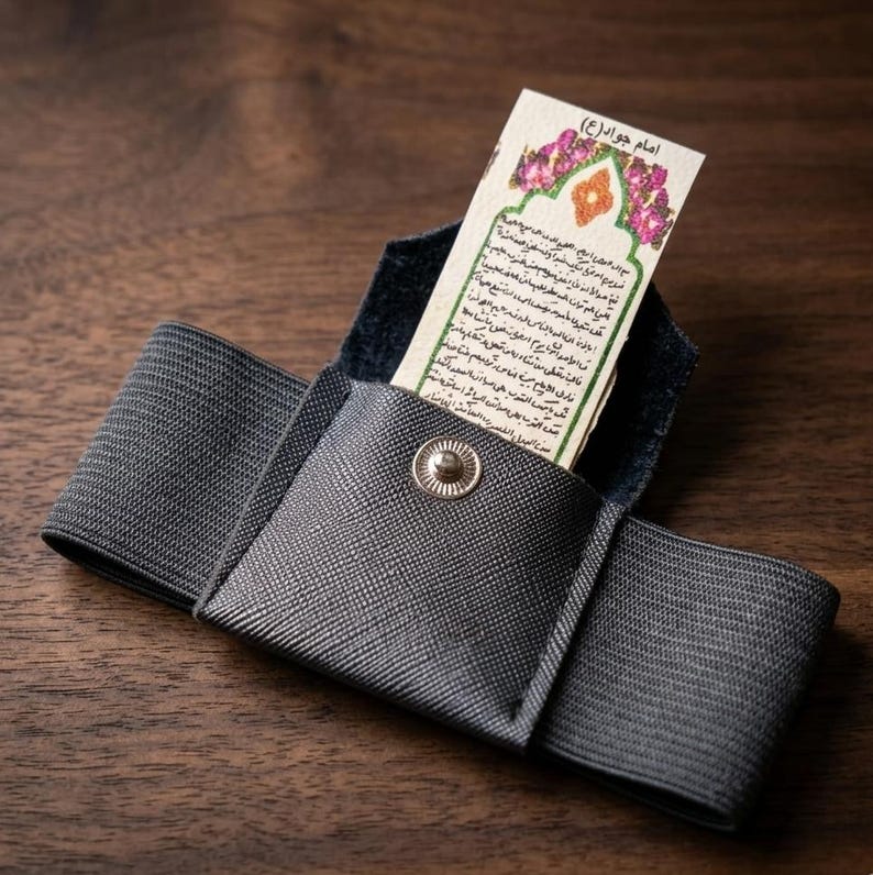 May include: A gray fabric wallet with a snap closure, holding a small card with text and floral accents. The wallet has an elastic band and is set against a wooden surface.