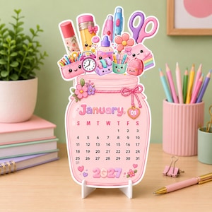 May include: A die-cut desk calendar for January 2027 shaped like a pink mason jar. The top features illustrations of school supplies including a pencil, scissors, and glue. The calendar displays the month, days of the week, and dates.