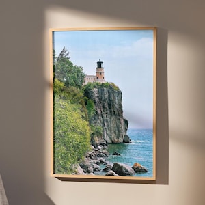 May include: A photograph of a lighthouse on a cliff overlooking a body of water. The lighthouse is a tall, white structure with a red roof and a black and white striped tower. The cliff is covered in green trees and bushes. The water is a deep blue color and the sky is a light blue color.