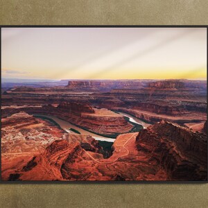 May include: A panoramic view of a desert landscape with a winding river snaking through the canyons. The sun casts long shadows across the red rock formations, creating a dramatic scene.