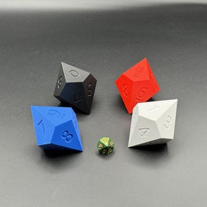 May include: Four polyhedral dice in black, red, blue, and white, with a small green and gold d20 die. The dice are numbered and have a geometric design, suitable for tabletop games.