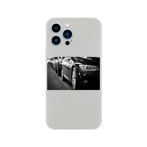 Puede incluir: Una funda de teléfono en blanco y negro con una foto de un coche negro en una fila de coches. La funda del teléfono tiene un recorte para el objetivo de la cámara con tres lentes.