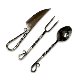 May include: A set of three handcrafted metal utensils: a knife, fork, and spoon. Each piece features a twisted handle design and a decorative loop at the end. The knife has a sharp blade, and the fork has two tines.
