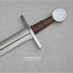 May include: A steel sword featuring a straight crossguard, a brown leather-wrapped grip, and a round polished pommel. The blade has a central fuller running down its length. Text at the bottom reads: Custom Sword, 14th century.