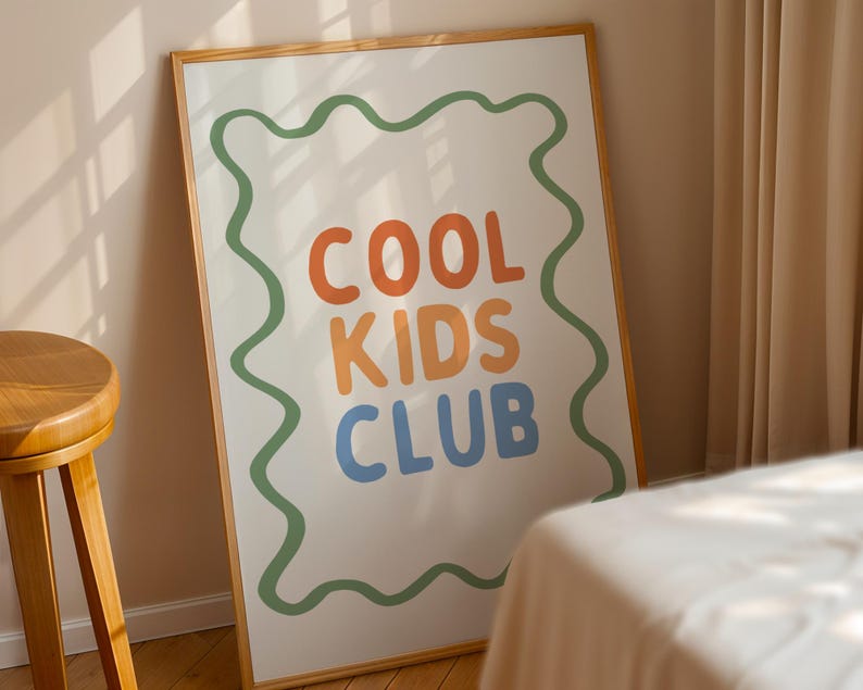 May include: A framed poster with the words "COOL KIDS CLUB" in orange, yellow, and blue, outlined by a green wavy border. The poster is displayed against a beige wall and a wooden frame.