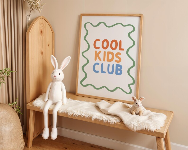 May include: A wooden bench with a white faux fur throw and two stuffed bunny rabbits. A framed print with the words "COOL KIDS CLUB" in orange, blue, and green is on the wall. The room has a neutral color palette.