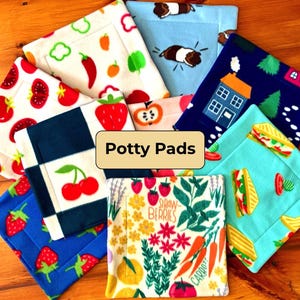 May include: A collection of colorful potty pads with various patterns, including fruits, vegetables, houses, and guinea pigs. The pads are square-shaped and made of soft fabric. The text "Potty Pads" is displayed on a beige background.