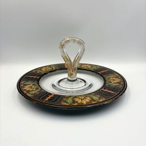 May include: A clear glass serving tray with a decorative handle. The tray features a black rim with gold, orange, and green floral patterns. The handle has gold accents.