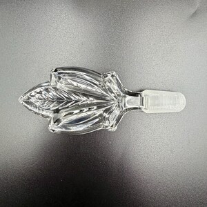 K&ouml;nnte beinhalten: Klarer Glasflaschenverschluss mit Blattform. Der Verschluss hat ein detailliertes Bl&auml;ttermuster und ein konisches Ende zum Einsetzen in eine Flasche. Das klare Glas reflektiert das Licht. F&uuml;r dekorative Zwecke.