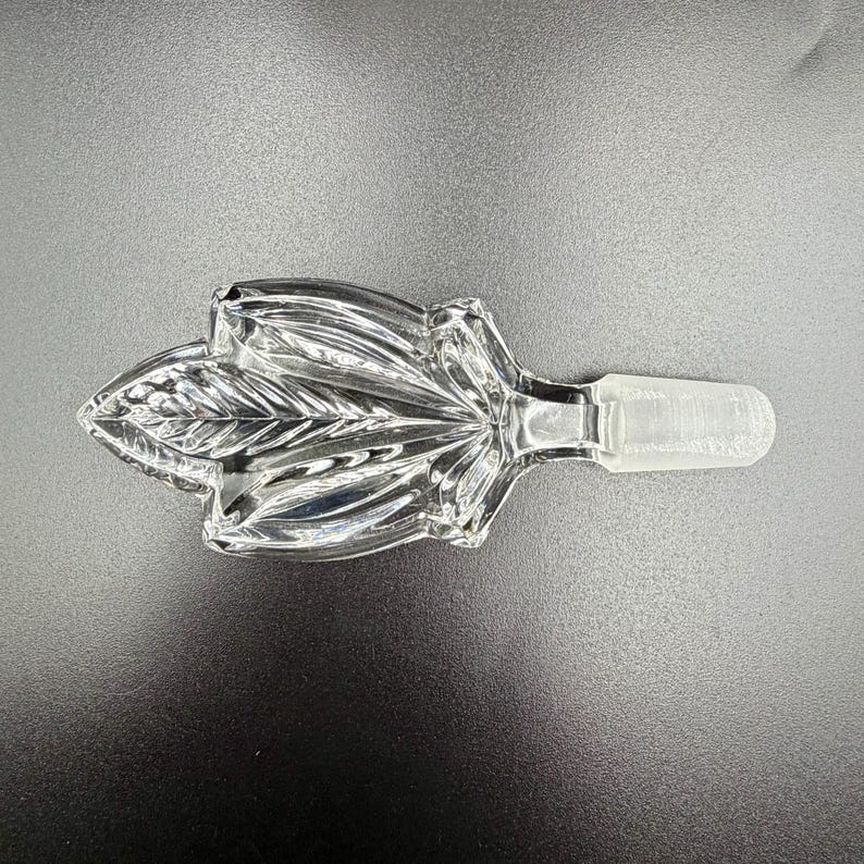K&ouml;nnte beinhalten: Klarer Glasflaschenverschluss mit Blattform. Der Verschluss hat ein detailliertes Bl&auml;ttermuster und ein konisches Ende zum Einsetzen in eine Flasche. Das klare Glas reflektiert das Licht. F&uuml;r dekorative Zwecke.