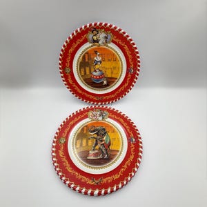 May include: Two round metal plates with red borders featuring white stripes. The top plate shows a duck balancing on a ball. The bottom plate depicts an elephant standing on a small pedestal. Both plates have gold filigree and circus-themed illustrations.