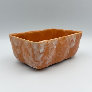May include: A rectangular ceramic bowl with a vibrant orange glaze and a white, mottled, cloud-like pattern along the exterior sides. The bowl features a smooth, glossy finish and a deep, open interior, showcasing a consistent color palette.