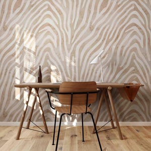 May include: A wooden desk with a brown leather bag hanging on the side. A wooden chair with black metal legs sits in front of the desk. The wall behind the desk is covered in a white and brown zebra print wallpaper.