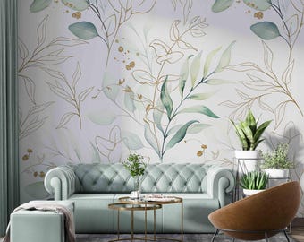 May include: A living room interior design with a light green sofa, a brown leather armchair, and a gold metal coffee table. The wall is decorated with a wallpaper featuring a watercolor pattern of green leaves and gold lines.