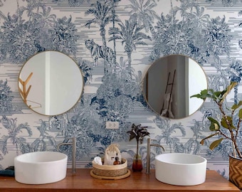 Könnte beinhalten: Ein Badezimmer mit einem Holzwaschtisch, zwei weißen Waschbecken und runden Spiegeln. Die Tapete zeigt eine blau-weiße Dschungelszene mit Tigern. Rechts steht eine Pflanze in einem geflochtenen Korb.