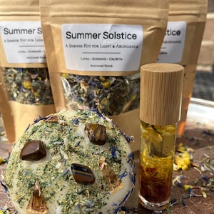 May include: A spherical white candle topped with dried herbs, blue flower petals, and brown tiger eye stones, next to a glass roller bottle with a bamboo cap and a brown liquid, and three brown paper pouches labeled Summer Solstice.