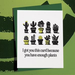 May include: A white greeting card with a green envelope. The card features black illustrations of various potted cacti and succulents. The text reads, "I got you this card because you have enough plants."